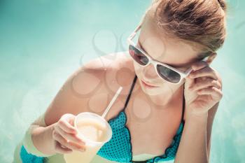Little blond girl with cocktail and sunglasses in swimming pool, vintage toned photo filter effect