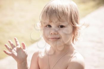 Outdoor closeup portrait of cute smiling Caucasian blond baby girl saying hello. Vintage toned photo with retro toning filter effect