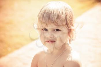 Outdoor close-up portrait of cute smiling Caucasian blond baby girl. Vintage toned photo with orange toning filter effect