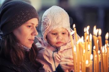 Mother and little blond Caucasian daughter with candles in Orthodox Russian Church. Vintage retro tonal correction photo filter