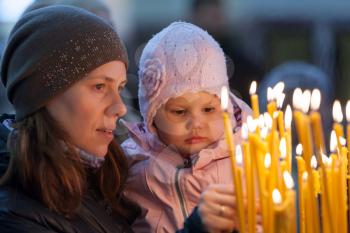 Mother and her little blond Caucasian girl with candles in Orthodox Russian Church