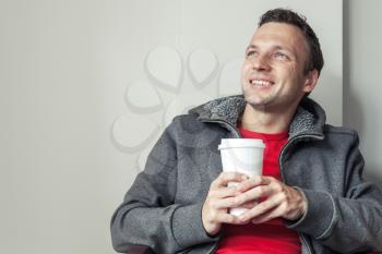 Portrait of young Caucasian man sitting in cafe with paper cup of Coffee