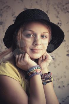 Retro stylized portrait of beautiful blond teenage girl in black hat and rubber loom bracelets. Vintage toned photo filter, instagram style effect