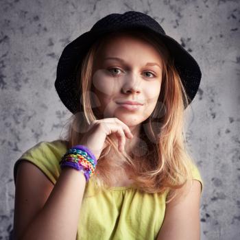 Portrait of beautiful blond teenage girl in black hat and rubber loom bracelets. Vintage toned photo filter, instagram style effect