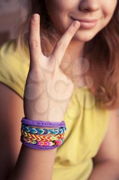 Caucasian girl showing two fingers with colorful rubber rainbow loom bracelets on her wrist, trendy teenagers fashion accessories. Vintage retro tonal photo filter correction
