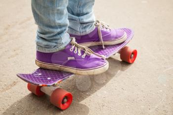 Young skateboarder in gumshoes and jeans standing on his skate. Close-up fragment of skateboard and feet