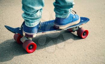 Young skateboarder in gumshoes and jeans standing on his skate. Close-up fragment of skateboard and feet, photo with retro tonal correction, instagram old style