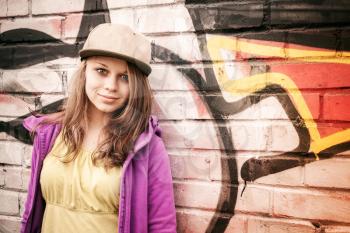 Blond stylish teenage girl stands near urban wall with graffiti, photo with warm retro tonal correction effect, instagram old style filter