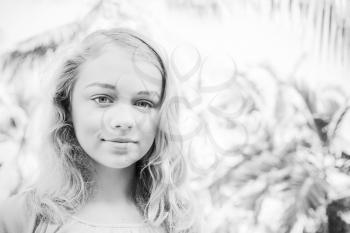 Blond beautiful girl teenager closeup outdoor summer portrait with palms on a background, monochrome retro style photo filter effect