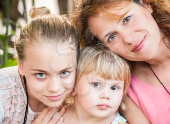 Outdoor summer closeup portrait of a real Caucasian family, young mother with her two daughters