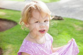 Outdoor portrait of cute smiling Caucasian blond baby girl in a summer park