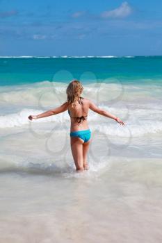 Happy teenage girl goes in the ocean water under deep blue sky, back view