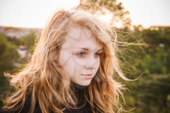 Outdoor closeup portrait of beautiful teenage Caucasian blond girl with bright evening sunlight back light