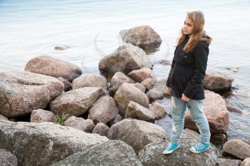 Beautiful blond Caucasian teenage girl walking on coastal stones on the lake coast in Finland