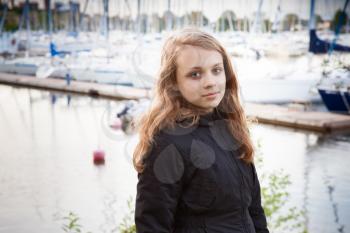 Portrait of beautiful teenage Caucasian blond girl on the lake coast with pier and yachts on blurred background