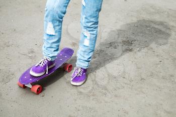 Teenager feet in jeans and gumshoes with skateboard on gray asphalt, selective focus