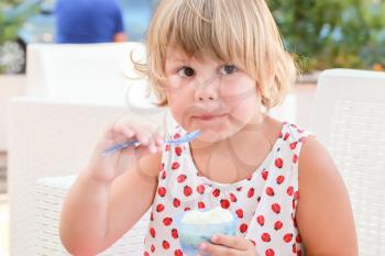 Blond Caucasian baby girl eats frozen yogurt, close-up outdoor portrait with natural light