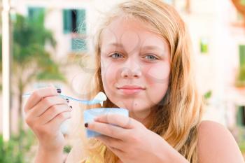 Blond Caucasian teenage girl eats frozen yogurt, close up outdoor portrait with natural light