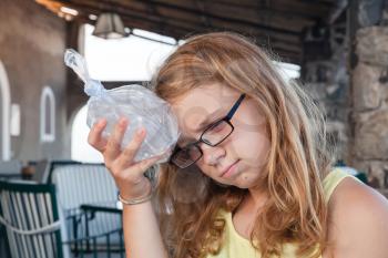Blond teenage Caucasian girl puts ice in a plastic bag to the head