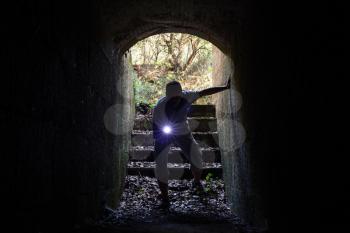 Young man with a flashlight enters the stone tunnel and looks in the dark