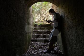 Young man works on a smart-phone in dark stone tunnel