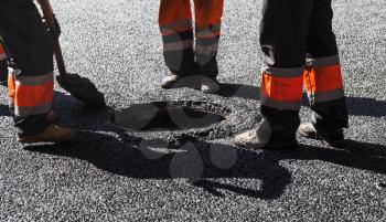 Men at work, urban road under construction, asphalting in progress, workers near sewer manhole