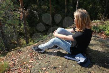 Blond Caucasian teenage girl sits in European forest