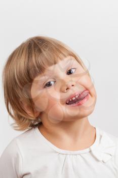 Cute Caucasian little girl shows tongue, closeup studio portrait on light gray background