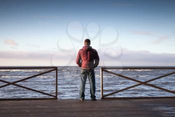 Young man looking on the sea from wooden pier at morning. Rear view photo
