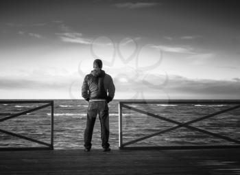 Young man looking on the sea from wooden pier. Rear view, black and white photo
