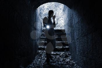 Young man with radio set and flashlight enters the stone tunnel and looks in the dark, monochrome photo