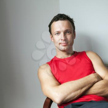 Young Caucasian man in red sporty shirt sitting with crossed arms