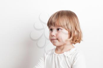Little blond Caucasian girl over white wall background, studio portrait