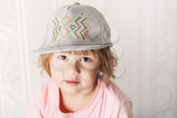 Closeup portrait of cute Caucasian blond baby girl in pink t-shirt and gray cap
