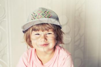 Closeup portrait of smiling cute Caucasian blond baby girl in gray cap, warm vintage tonal correction photo filter