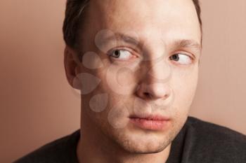 Young serious Caucasian man looking left, close-up studio portrait over gray wall background