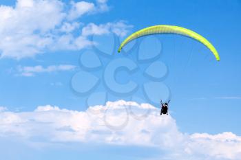 Paragliders in bright blue sky with clouds, tandem of instructor and beginner