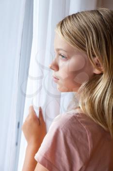 Closeup vertical portrait of beautiful blond Caucasian girl standing near a window with white curtains