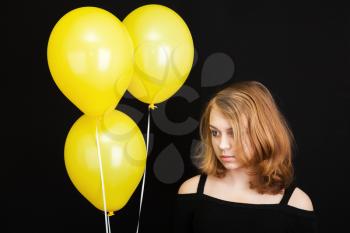 Portrait of beautiful sad teenage Caucasian blond girl with yellow balloons