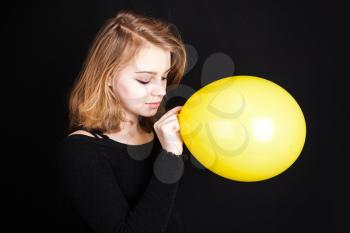 Studio portrait of teenage Caucasian blond girl with yellow balloon over black background