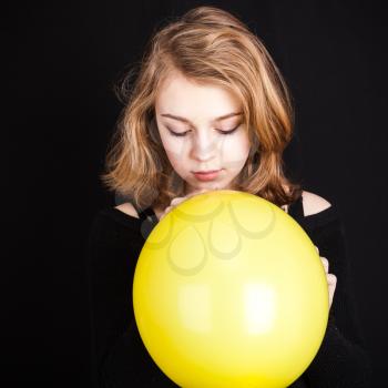 Studio portrait of teenage Caucasian blond girl with yellow balloon on black background