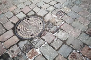 Round steel sewer manhole on cobblestone road