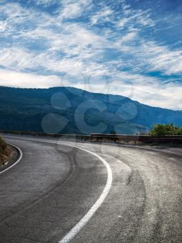 Turning rural road with blue mountains and cloudy sky on a background