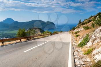 Mountain road with blue cloudy sky and sea on a background. Adriatic sea coast, Montenegro