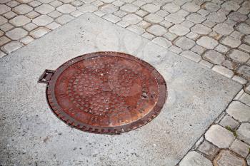 Old rusted sewer manhole on the cobblestone road