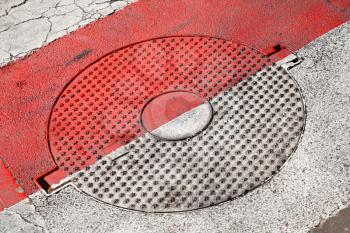 Closed round sewer manhole with stars pattern under red and white road marking
