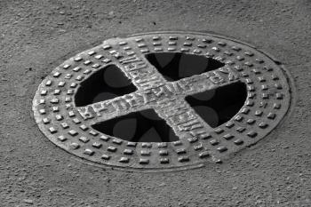 Round hatch in urban asphalt road pavement. Russian relief text on the cap means Sewerage