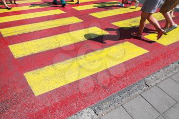 Pedestrian crossing road marking with yellow and red lines on asphalt and walking people legs