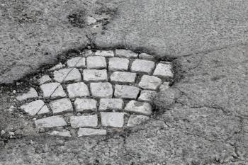 Pothole with old gray stone pavement on damaged urban asphalt road