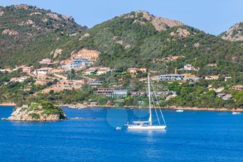 Coastal landscape of Porto-Vecchio bay, Corsica island, France. White sailing yacht go near small rocky island